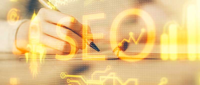 Main écrivant sur un carnet avec le mot SEO et des graphiques numériques en surimpression